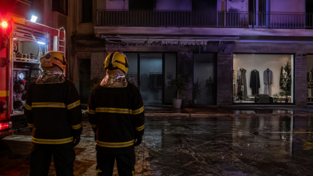 Πυροσβεστική επιχείρηση έξω από κατάστημα ρούχων τη νύχτα σε συμβολική εικόνα