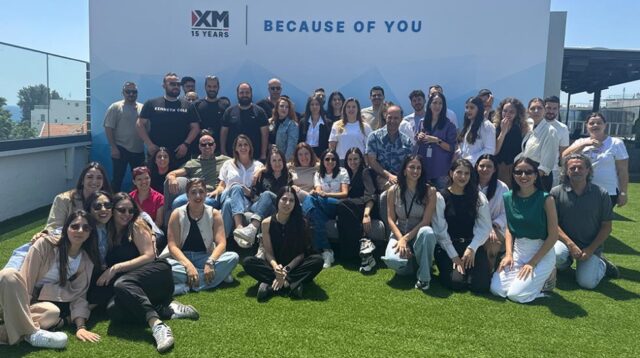 Ομαδική φωτογραφία στον χώρο της XM με το εταιρικό λογότυπο στο φόντο
